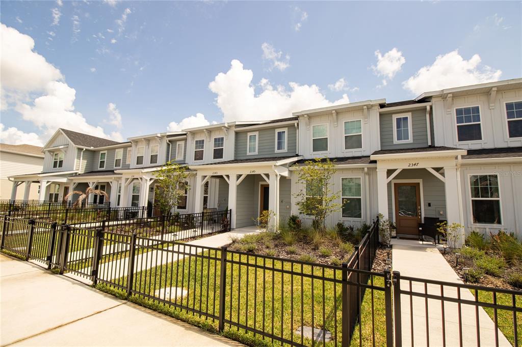 A row of two-story townhouses with gray siding, white trim, and black metal fences — 2345 SOUTHBURY, KISSIMMEE, FL