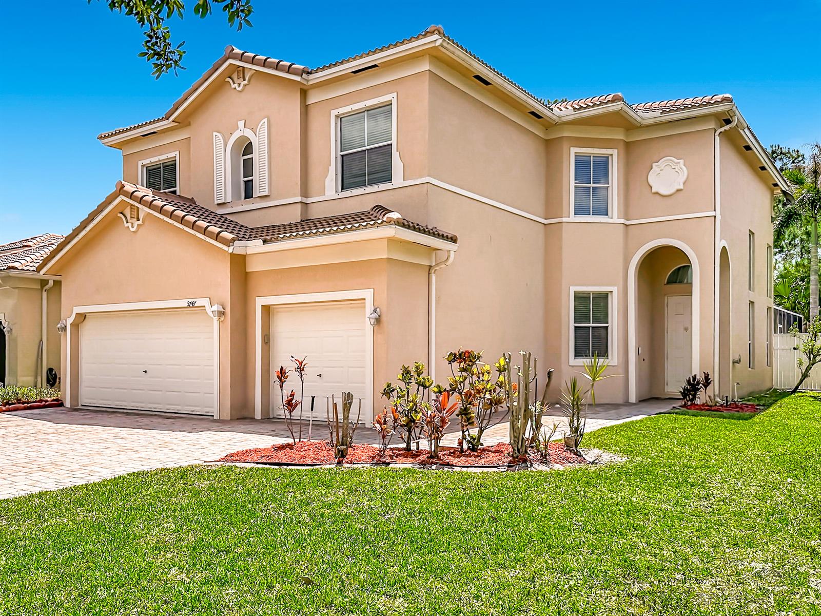 A two-story tan stucco house features a three-car garage and a landscaped front yard — 5747 Sunberry Circle, Fort Pierce FL 34951, FORT PIERCE, FL
