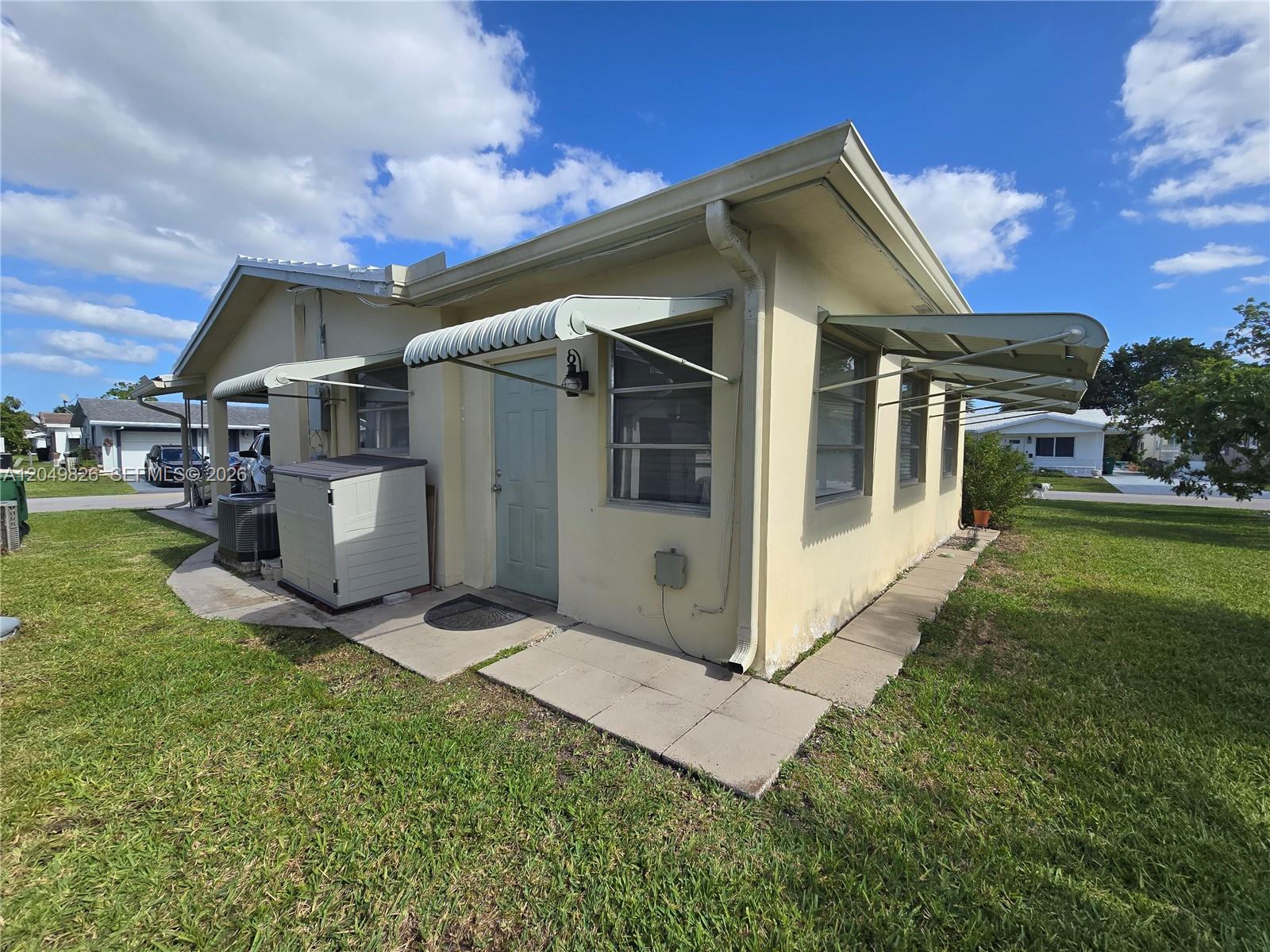 The exterior of a light yellow house features metal awnings over the windows and door — 4805 NW 45th Ave, Tamarac FL 33319, TAMARAC, FL