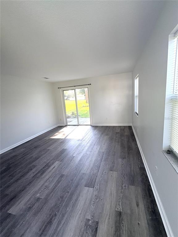 An empty room features gray wood-look flooring, white walls, a sliding glass door, and windows — 2829 NORDMAN AVENUE, NEW SMYRNA BEACH, FL