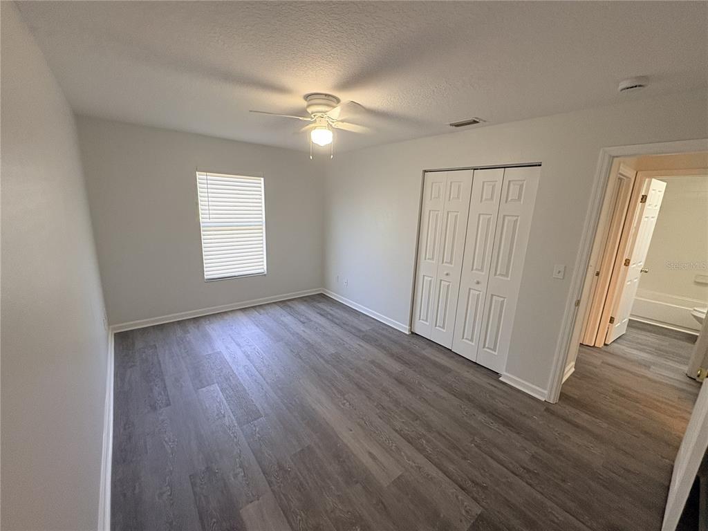 A bedroom with gray wood-look flooring, white walls, a ceiling fan, and a closet — 2829 NORDMAN AVENUE, NEW SMYRNA BEACH, FL