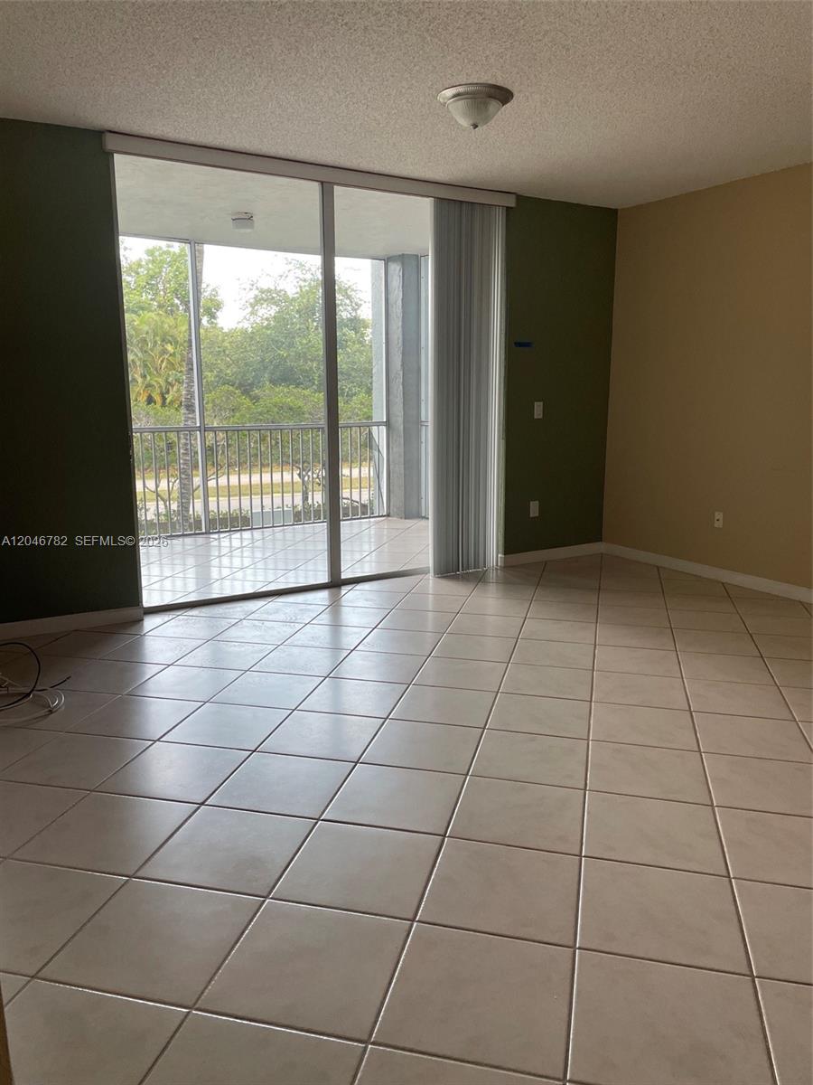 An empty room with light-colored floor tiles, green accent walls, and a sliding glass door — 9725 NW 52nd St # 210, Doral FL 33178, DORAL, FL