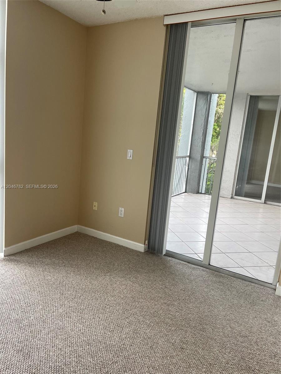 A room with beige walls and carpeted flooring features a sliding glass door to a balcony — 9725 NW 52nd St # 210, Doral FL 33178, DORAL, FL