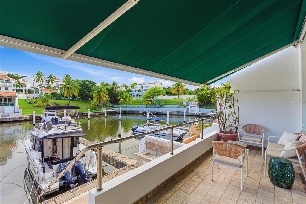 A balcony with outdoor furniture overlooks a marina with docked boats under a green awning — 25 PLAZA MAYOR, HUMACAO, PR