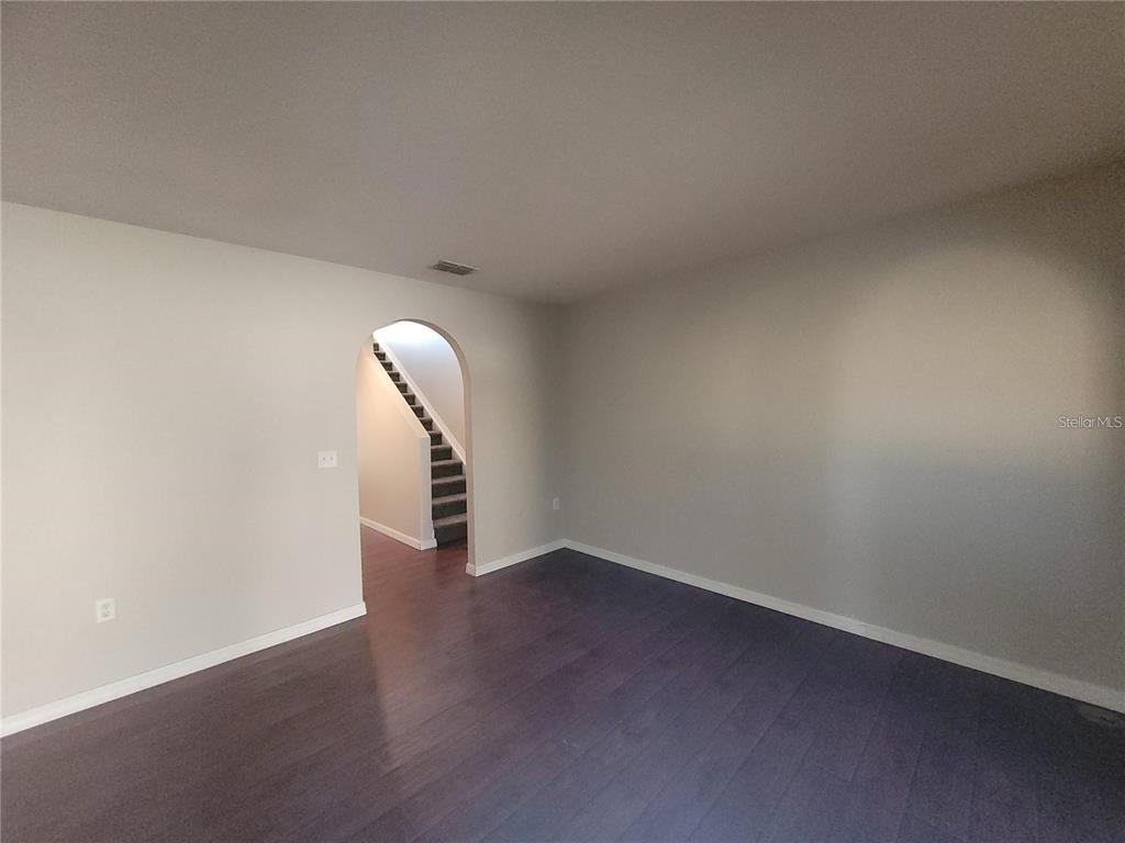 An empty room with dark wood flooring and an arched doorway leading to stairs — 3805 EXETER LANE, LAKELAND, FL