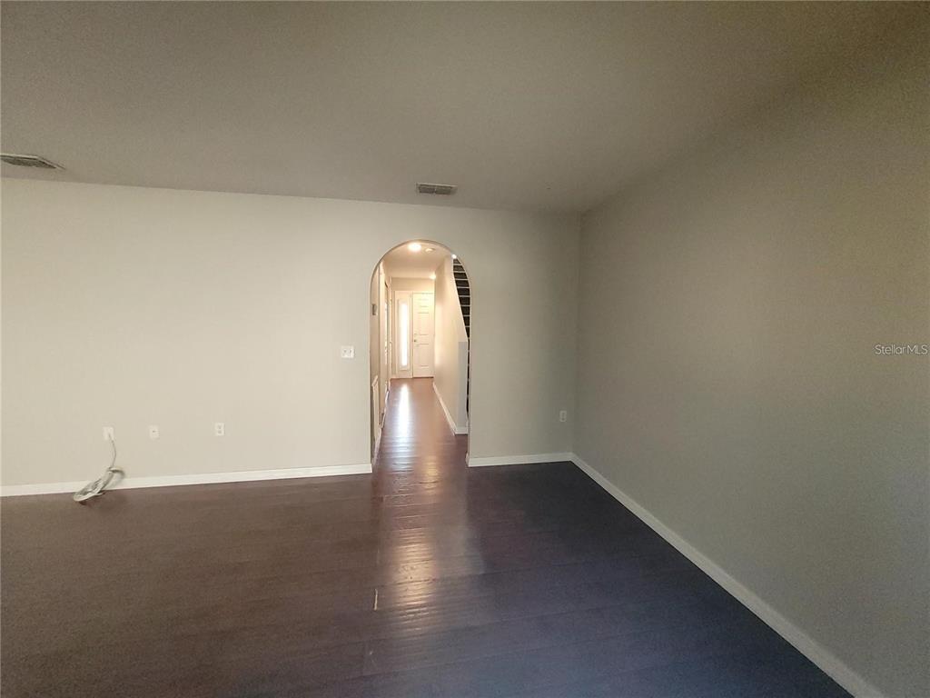 An empty room with dark wood flooring leads through an arched doorway to a hallway — 3805 EXETER LANE, LAKELAND, FL