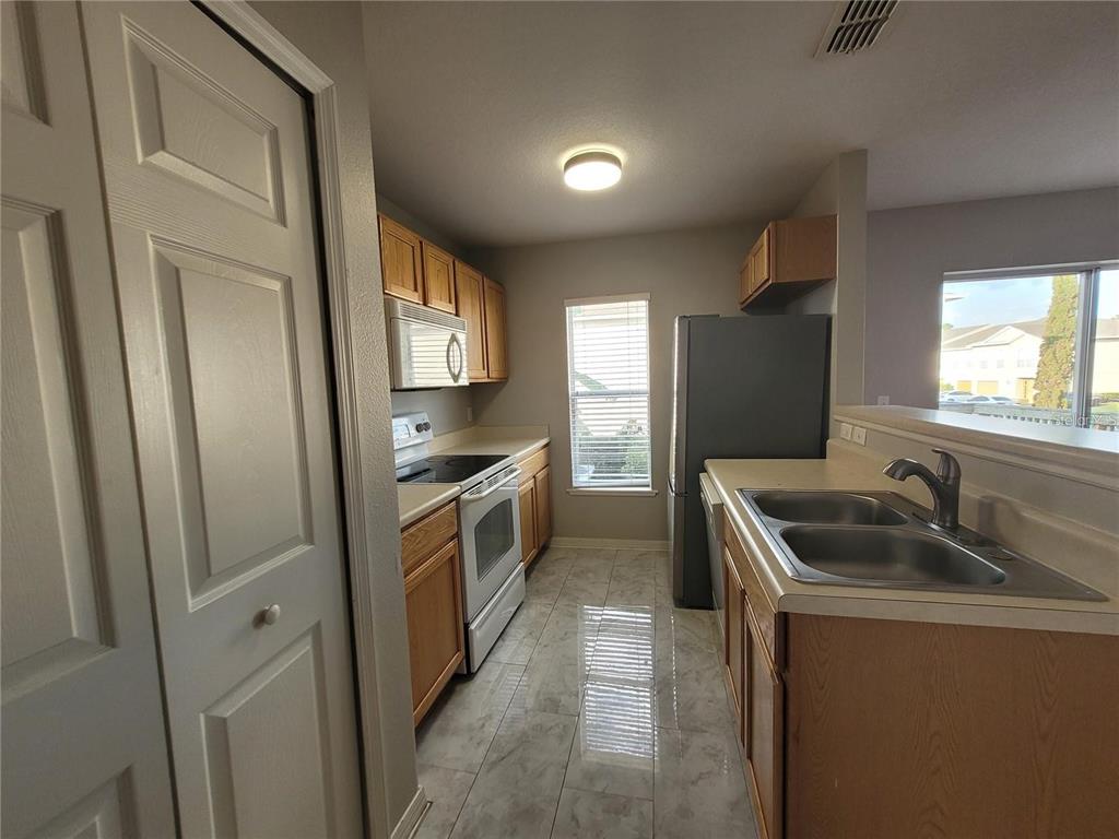 A kitchen features light wood cabinets, white appliances, a double sink, and tiled flooring — 3805 EXETER LANE, LAKELAND, FL