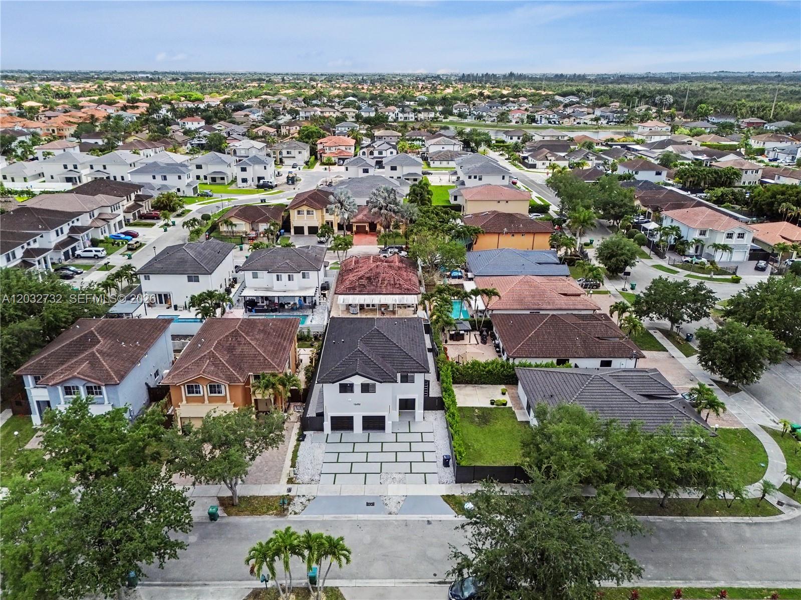 An aerial view shows a suburban neighborhood with detached houses, paved driveways, and green lawns — 15490 SW 18th Ln, Miami FL 33185, MIAMI, FL