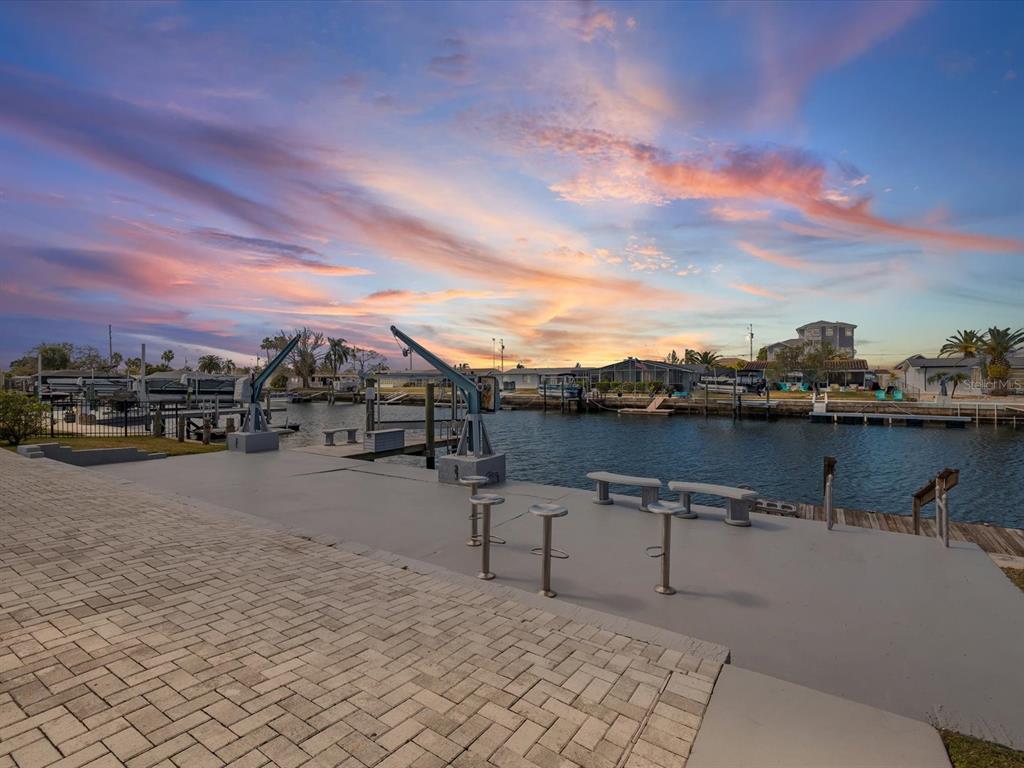 A paved patio overlooks a canal with a boat lift and a sunset sky — 12809 4TH ISLE, HUDSON, FL