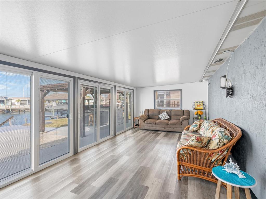 A sunroom with wood-look flooring, sliding glass doors, and two sofas overlooking a canal — 12809 4TH ISLE, HUDSON, FL
