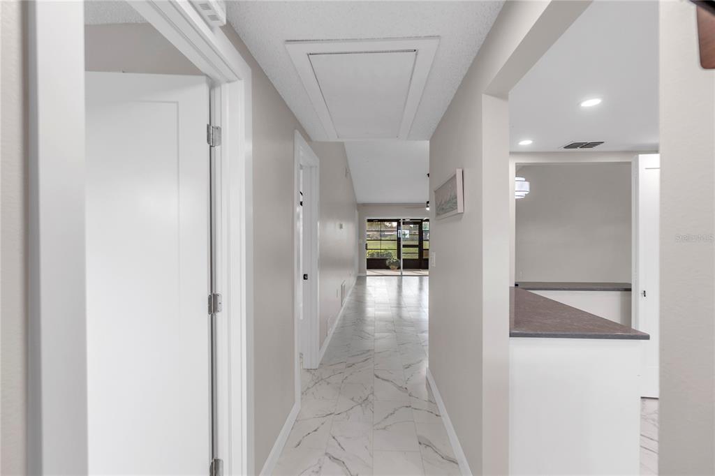 A hallway with white marble-look tile flooring leads toward a glass-enclosed patio area — 6135 HERITAGE LANE UNIT 6135, BRADENTON, FL
