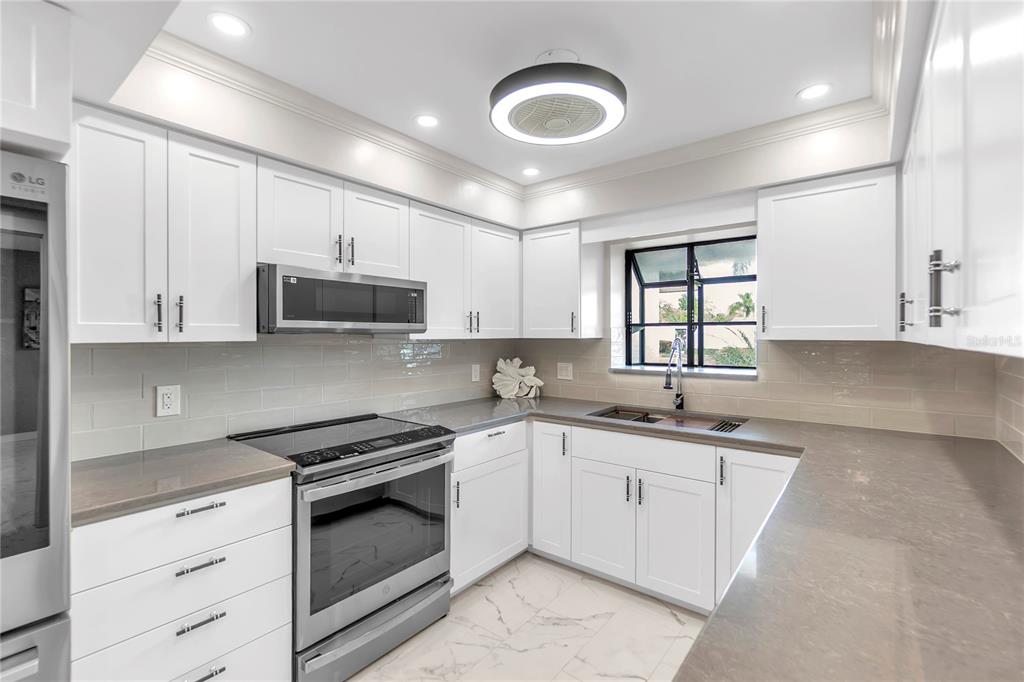A modern kitchen features white cabinetry, stainless steel appliances, gray countertops, and a tile backsplash — 6135 HERITAGE LANE UNIT 6135, BRADENTON, FL