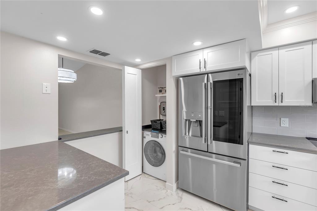 A kitchen features white cabinets, gray countertops, a stainless steel refrigerator, and an adjacent laundry closet — 6135 HERITAGE LANE UNIT 6135, BRADENTON, FL