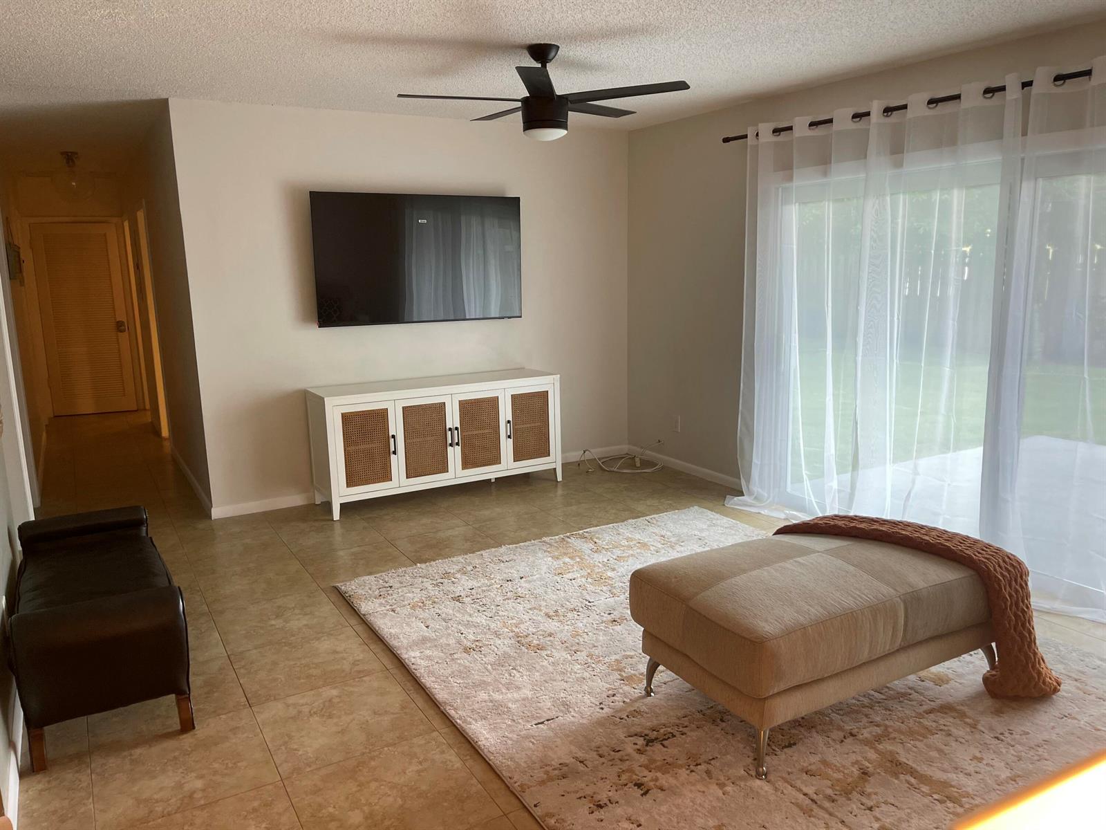 A living room features a wall-mounted television, a white media console, and a large ottoman — 187 Auburn Drive, FL 33460, FL