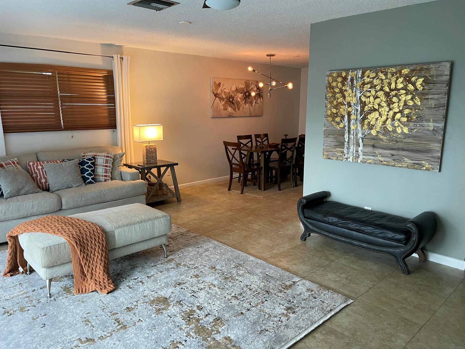 A living room with a sofa and ottoman flows into a dining area with wood furniture — 187 Auburn Drive, FL 33460, FL