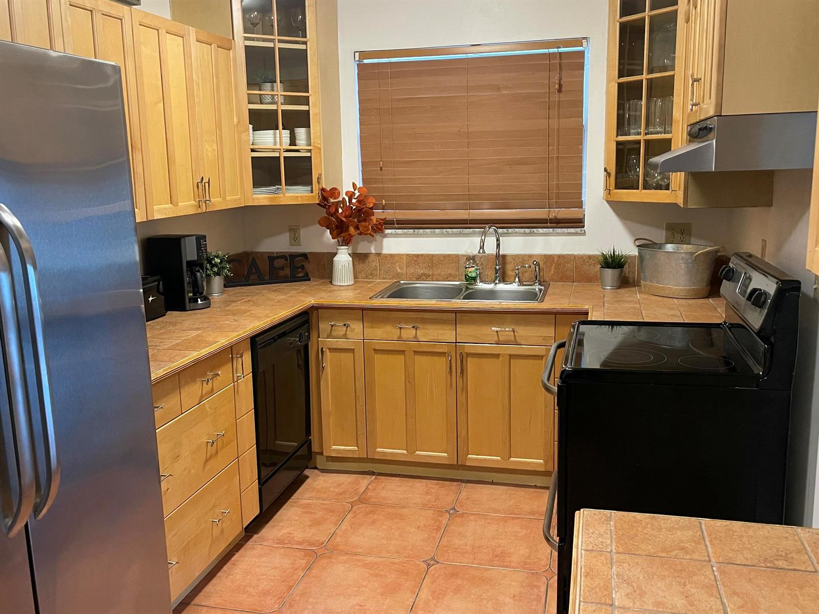 A kitchen features light wood cabinets, tile countertops, a double sink, and black appliances — 187 Auburn Drive, FL 33460, FL