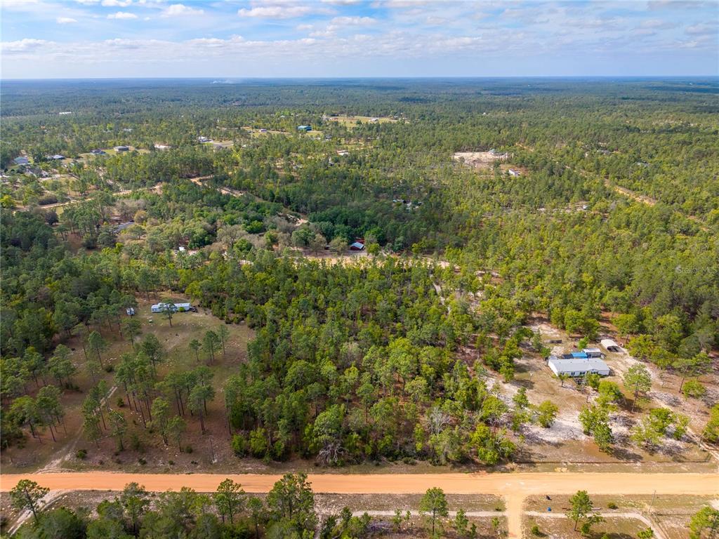 An aerial view shows a rural, wooded landscape with scattered houses and a dirt road — 230 MELROSE LANDING DRIVE, HAWTHORNE, FL