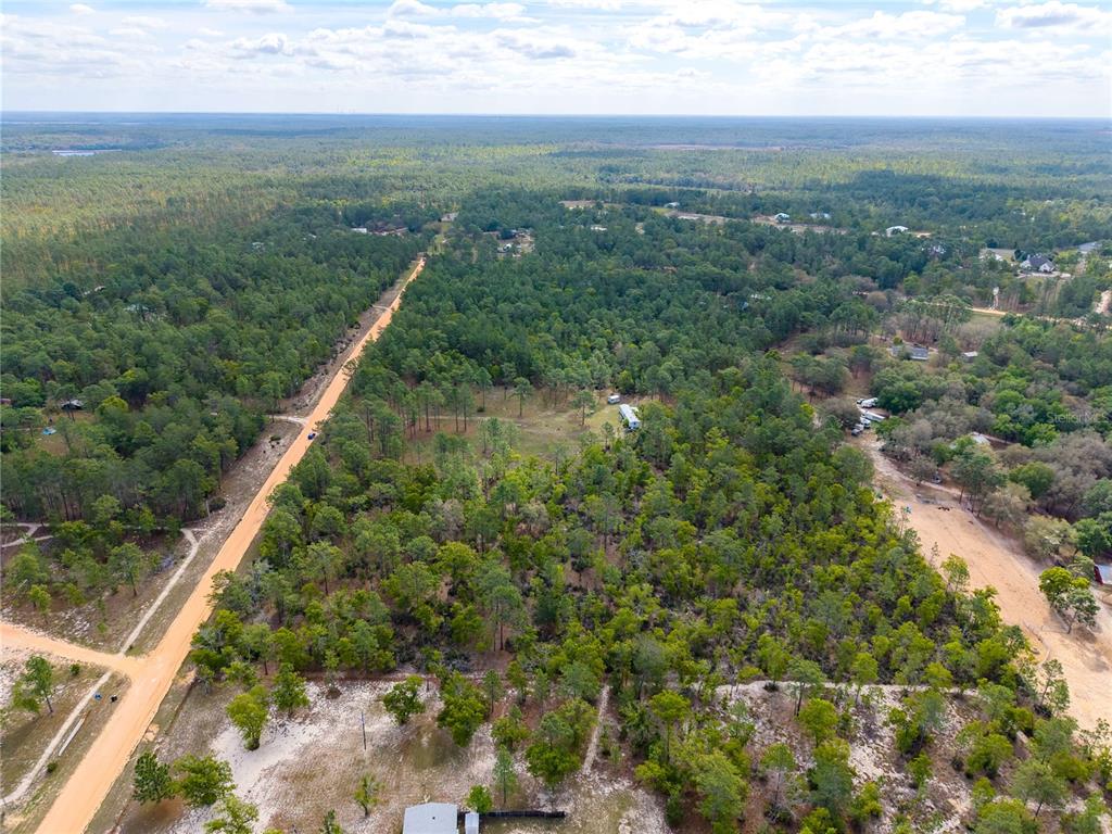 An aerial view shows a dirt road bordering a wooded lot with a small structure — 230 MELROSE LANDING DRIVE, HAWTHORNE, FL