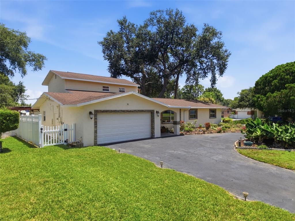 A two-story house with a white garage, asphalt driveway, and a large tree in front — 701 58TH AVENUE S, ST PETERSBURG, FL