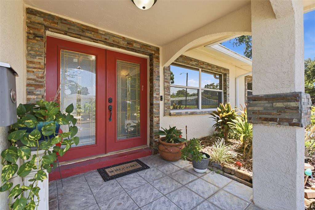 A front porch with a red double door, stone accents, and potted plants — 701 58TH AVENUE S, ST PETERSBURG, FL
