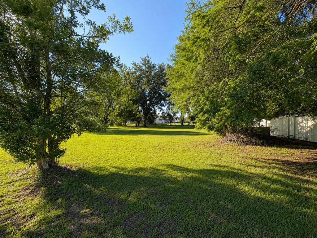A large, grassy backyard features several mature trees and a white fence on the right — SW 3RD CT, OCALA, FL