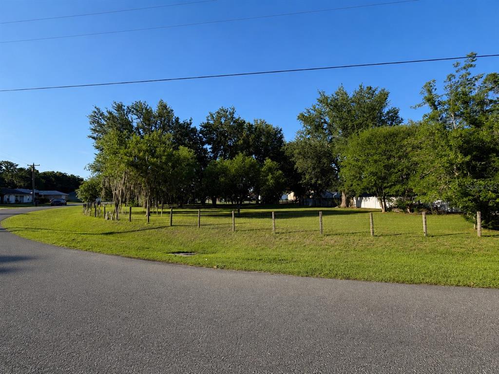 A large, grassy, fenced-in vacant lot with mature trees under a clear blue sky — SW 3RD CT, OCALA, FL
