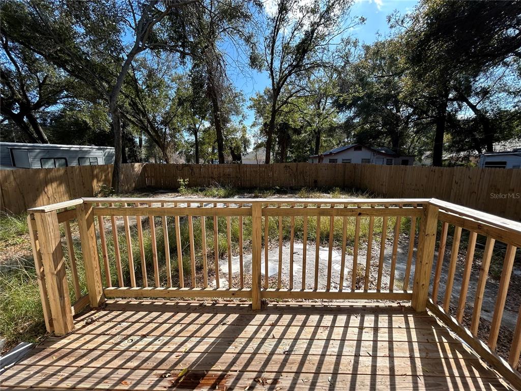 A wooden deck overlooks a fenced backyard with overgrown grass and mature trees — 2119 E ELLICOTT STREET, TAMPA, FL