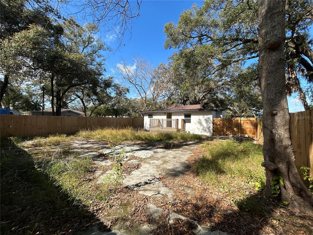A backyard features a concrete patio, overgrown grass, a wooden fence, and a small house — 2119 E ELLICOTT STREET, TAMPA, FL