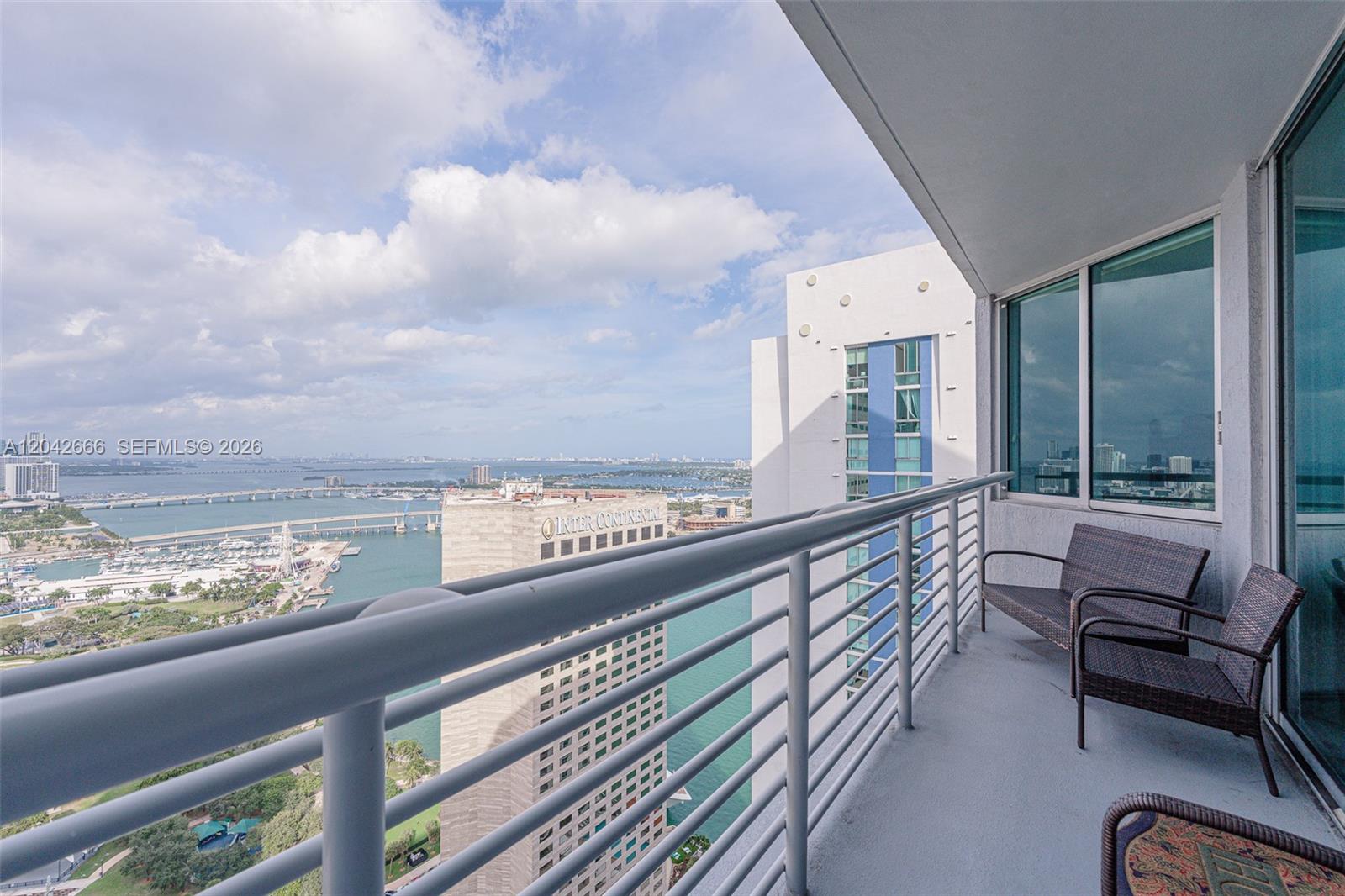 A high-rise balcony features metal railings, wicker chairs, and a view of the city skyline — 325 S BISCAYNE BLVD # 4222, Miami FL 33131, MIAMI, FL