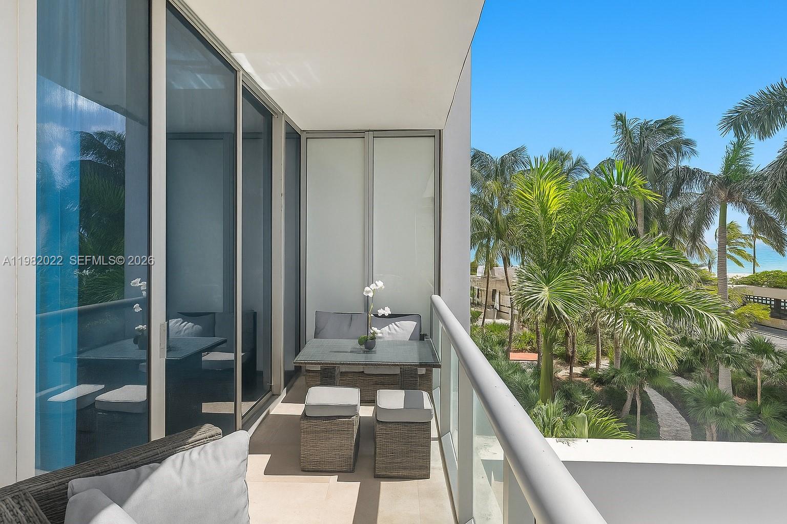 A balcony features a small dining set, glass railings, and a view of palm trees — 6799 Collins Ave # 209, Miami Beach FL 33141, MIAMI BEACH, FL