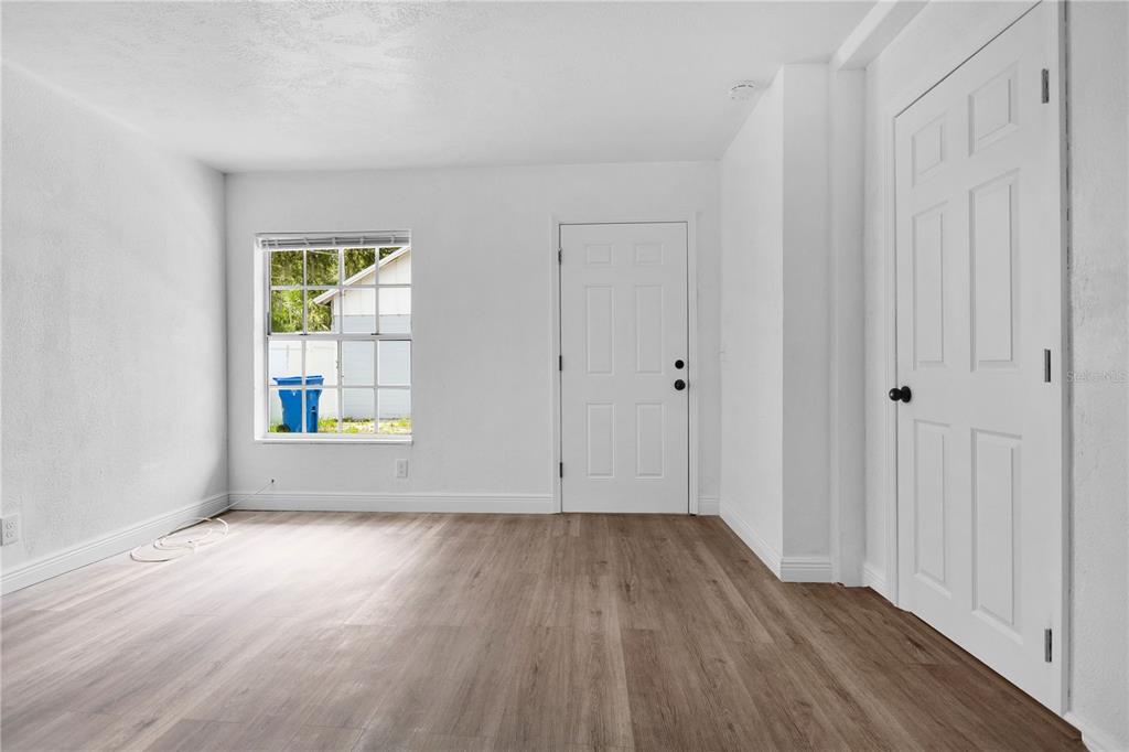 An empty room features white walls, wood-look flooring, a window, and two white doors — 1409 COLLEGE PARK LANE, TAMPA, FL