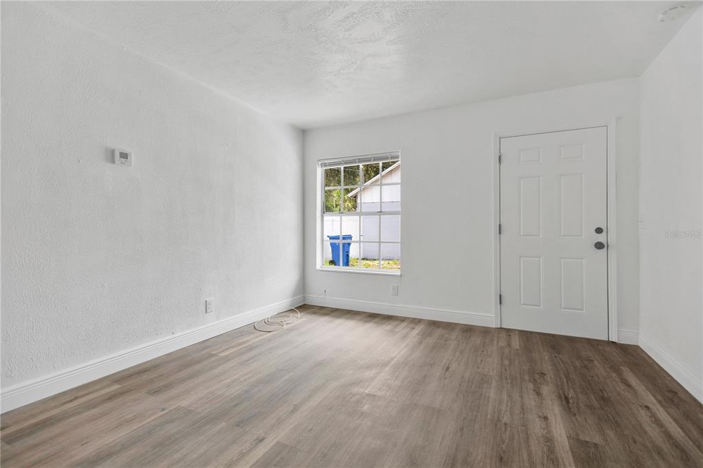 A bright, empty room features white walls, wood-look flooring, a single window, and a white door — 1409 COLLEGE PARK LANE, TAMPA, FL