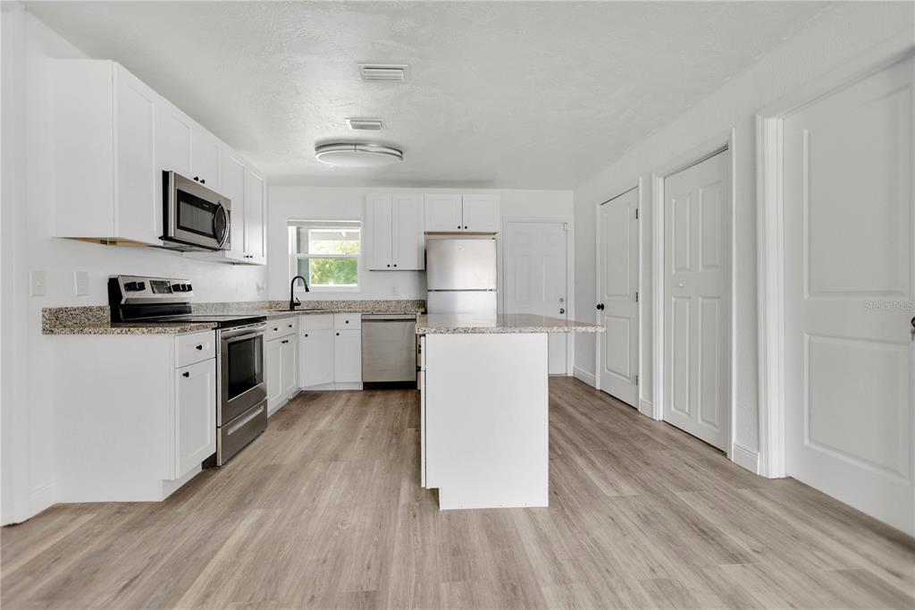 A kitchen features white cabinets, granite countertops, stainless steel appliances, and light wood-look flooring — 1409 COLLEGE PARK LANE, TAMPA, FL