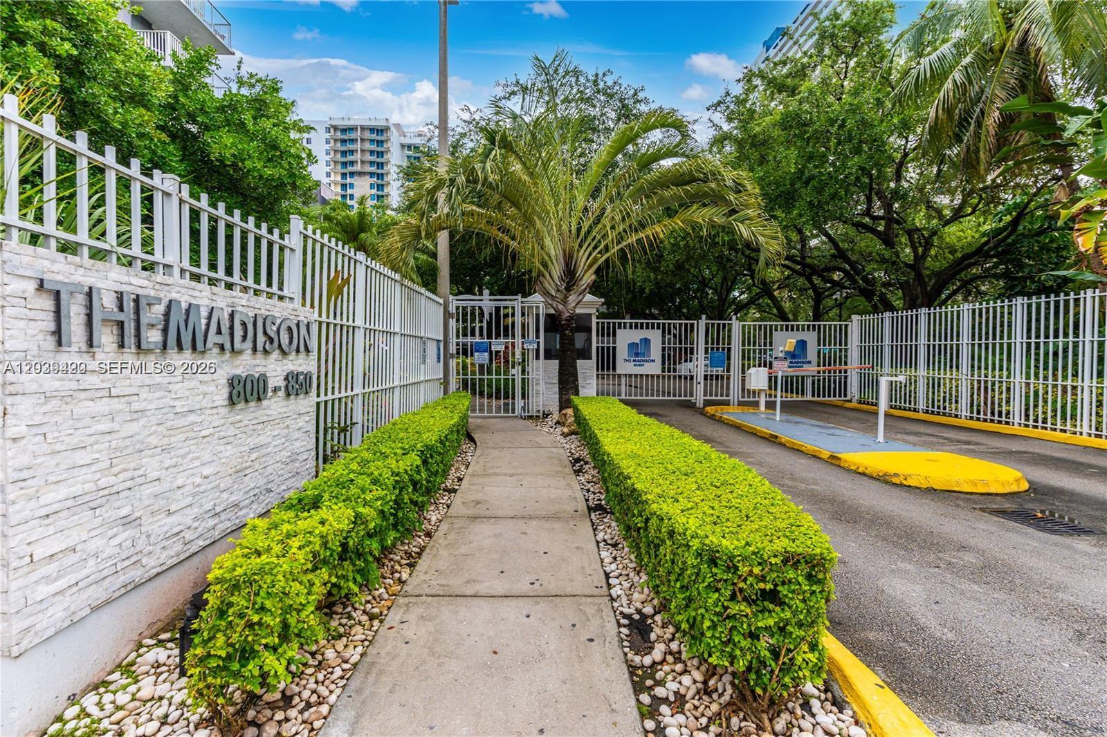 A gated entrance with a walkway, manicured hedges, and signage for The Madison — 800 N Miami Ave # 1008, Miami FL 33136, MIAMI, FL