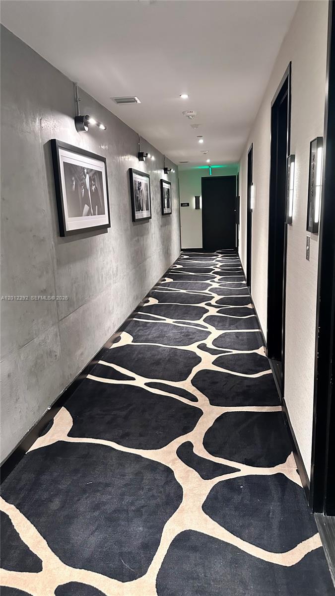 A hallway features a giraffe-patterned carpet, concrete-style walls, framed artwork, and recessed lighting — 20 NE 11 # 2212A, Miami FL 33132, MIAMI, FL