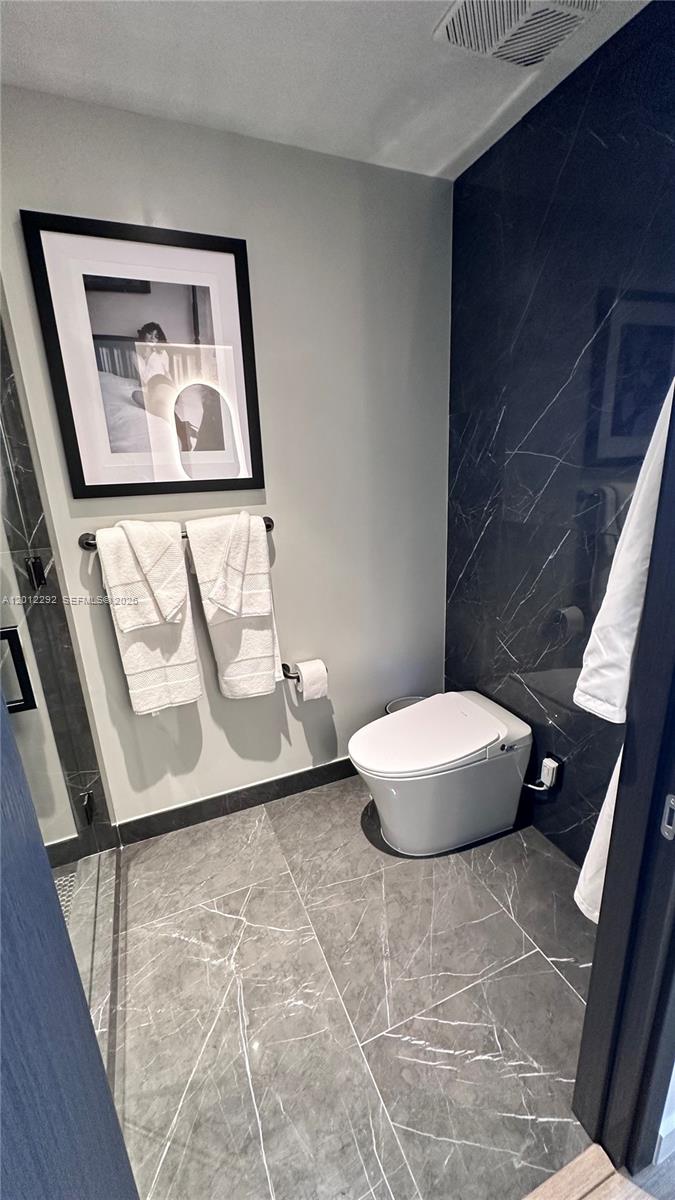 A modern bathroom features a wall-mounted toilet, gray marble-look tile flooring, and dark marble wall accents — 20 NE 11 # 2212A, Miami FL 33132, MIAMI, FL