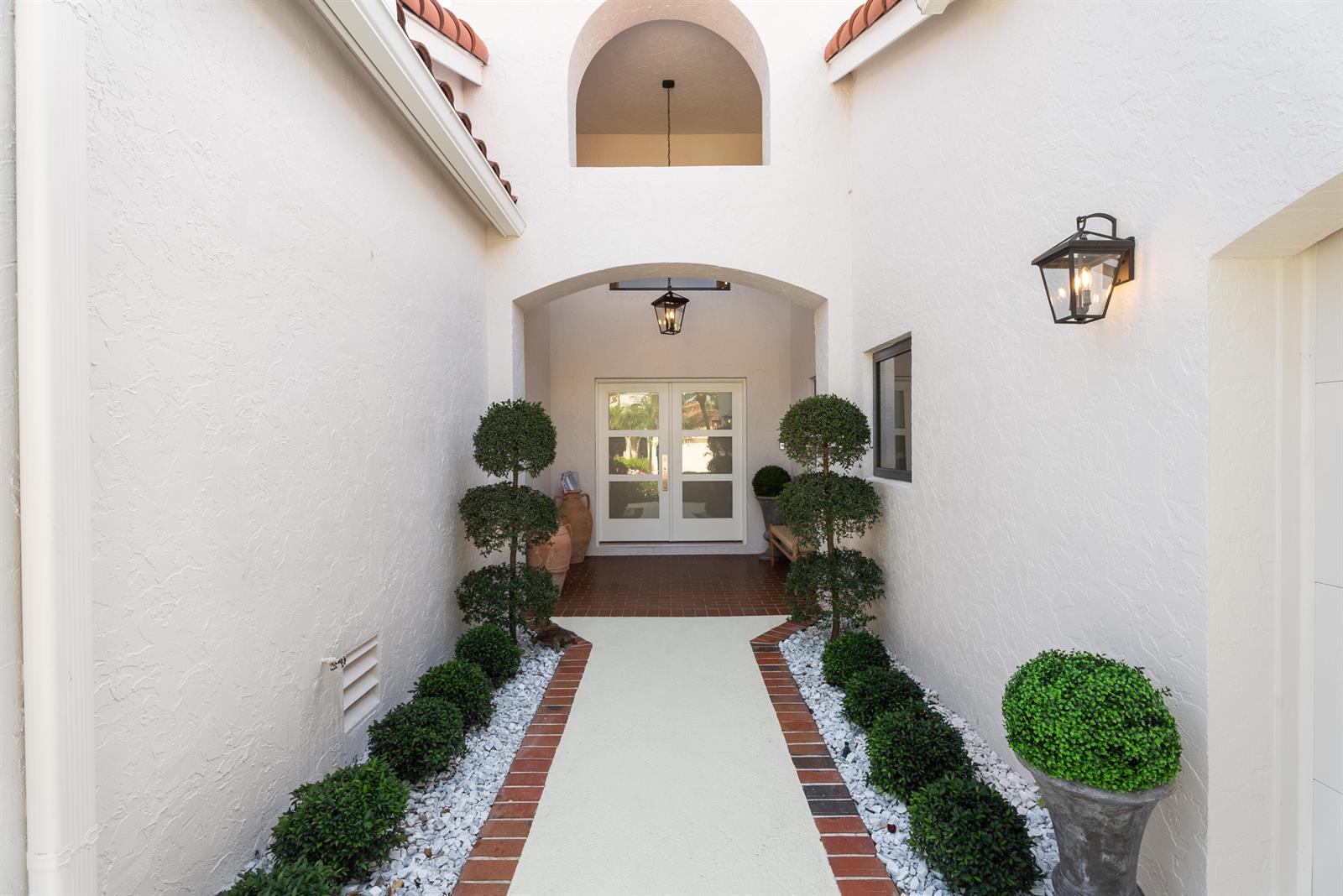 An outdoor entryway features a white stucco walkway flanked by manicured shrubs and brick borders — 16613 Hidden Cove Drive, Jupiter FL 33477, JUPITER, FL