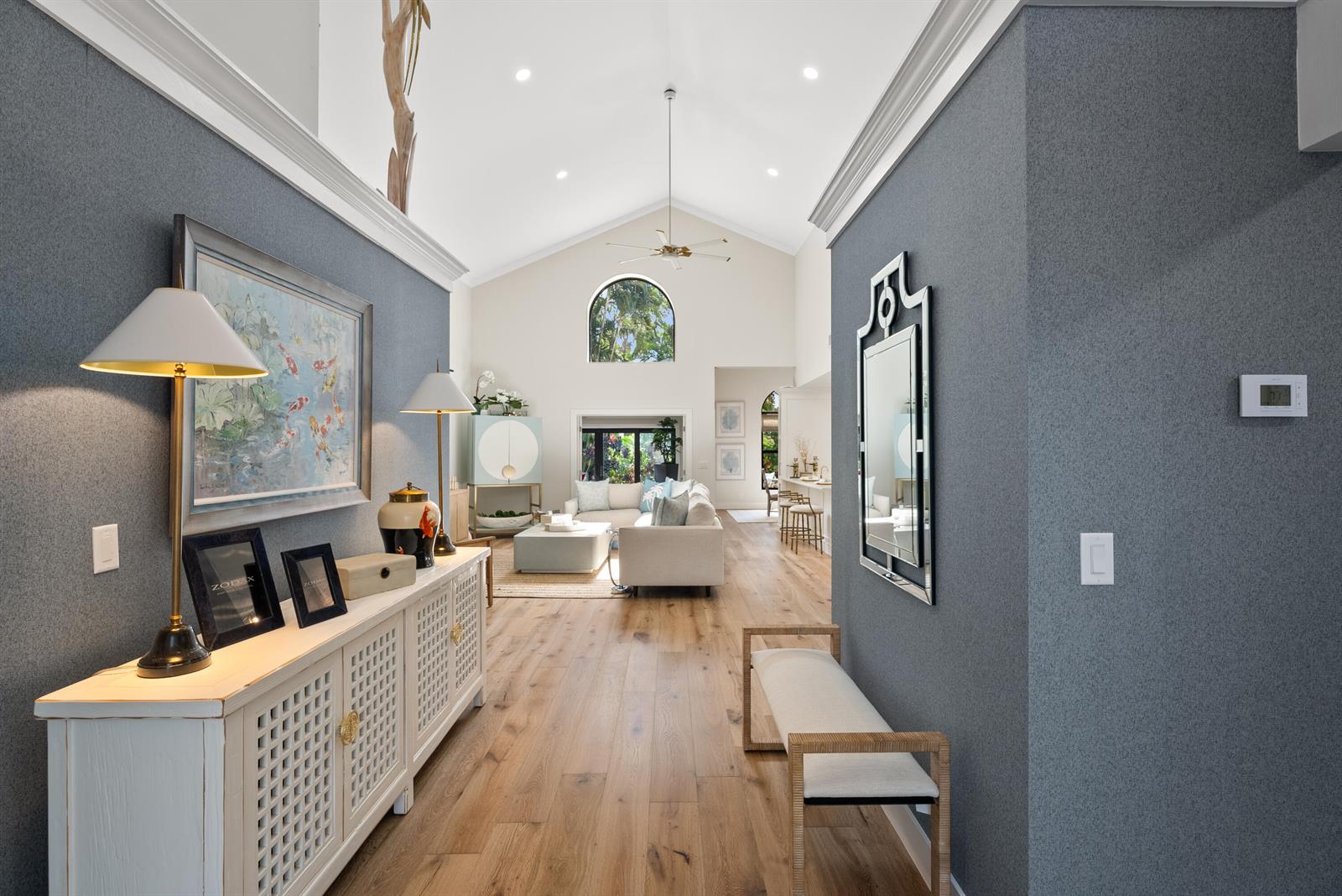 A hallway with blue textured walls leads into a bright living room with vaulted ceilings — 16613 Hidden Cove Drive, Jupiter FL 33477, JUPITER, FL