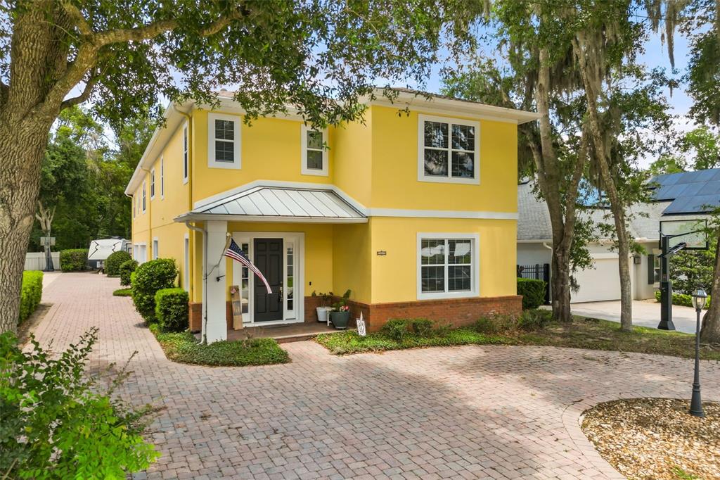 A two-story yellow house with a brick base, metal porch roof, and paved driveway — 161 VINE STREET, OVIEDO, FL