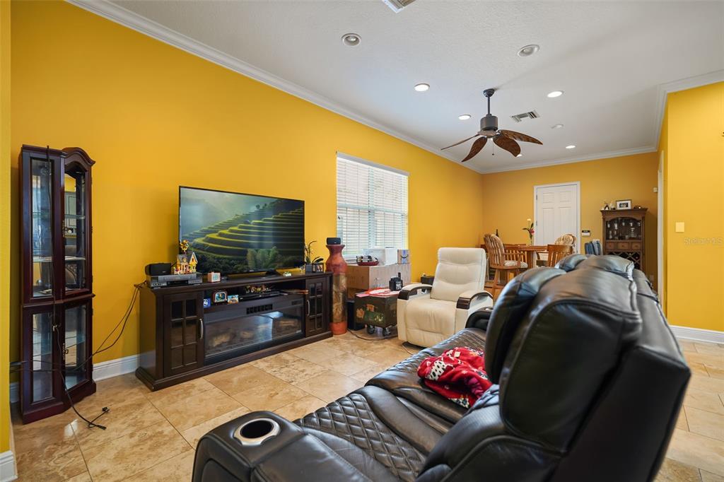 A living room with yellow walls, tile flooring, a black leather sofa, and a television — 161 VINE STREET, OVIEDO, FL