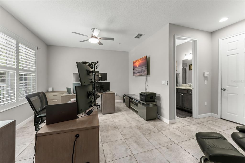 A home office features a multi-monitor desk setup, tile flooring, and an attached bathroom — 1457 LAKE GEORGE DRIVE UNIT 1457, LAKE MARY, FL