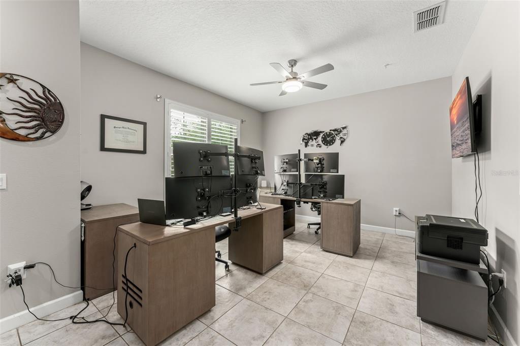 A home office features two desks with multiple computer monitors, tile flooring, and a ceiling fan — 1457 LAKE GEORGE DRIVE UNIT 1457, LAKE MARY, FL