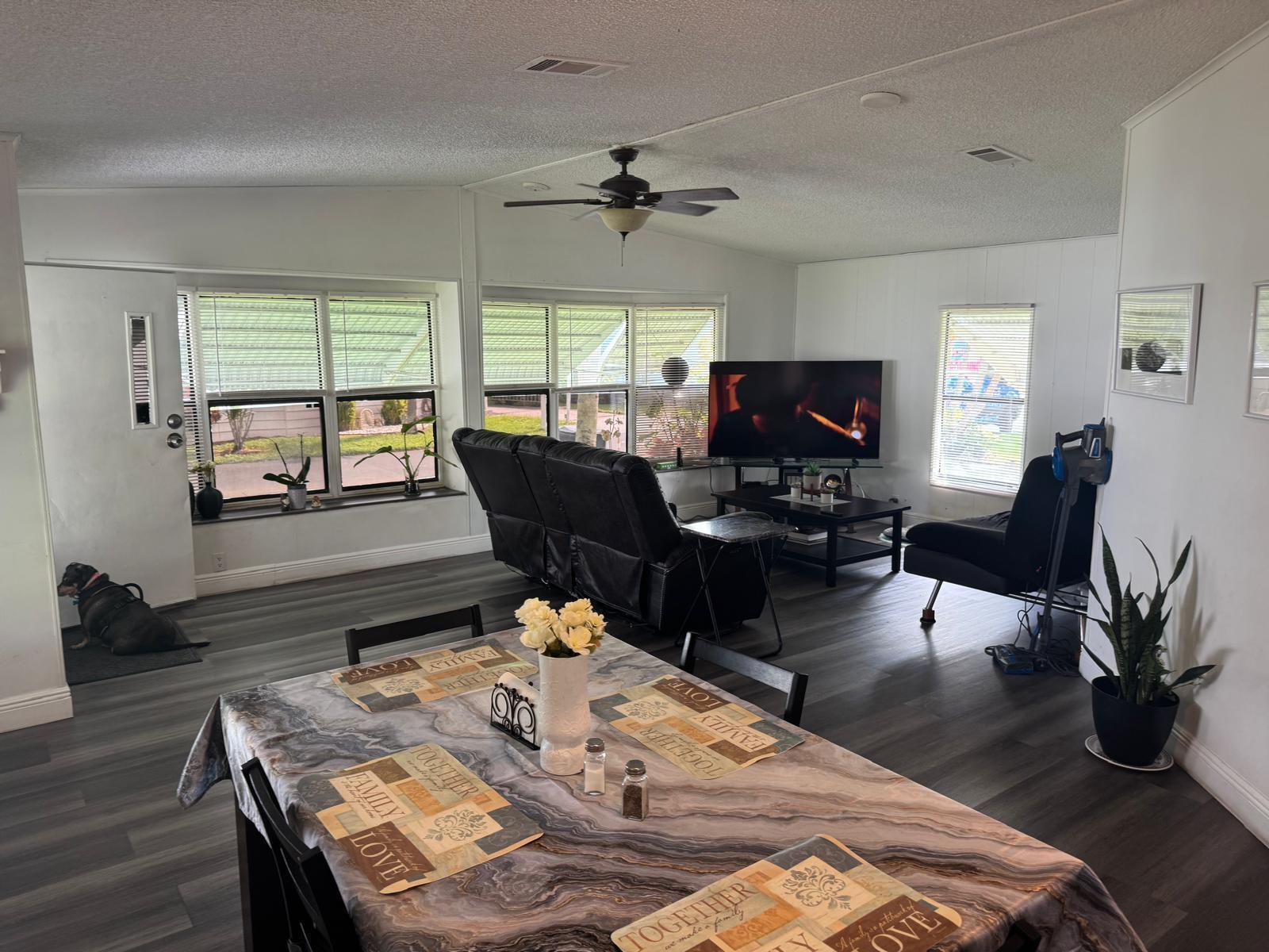 An open-concept living and dining area features wood-look flooring, a ceiling fan, and large windows — 6059 Palm Harbour Drive, Atlantis FL 33462, ATLANTIS, FL