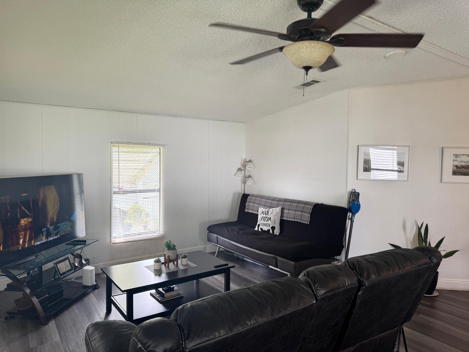 A living room features a black sofa, a coffee table, a television, and a ceiling fan — 6059 Palm Harbour Drive, Atlantis FL 33462, ATLANTIS, FL