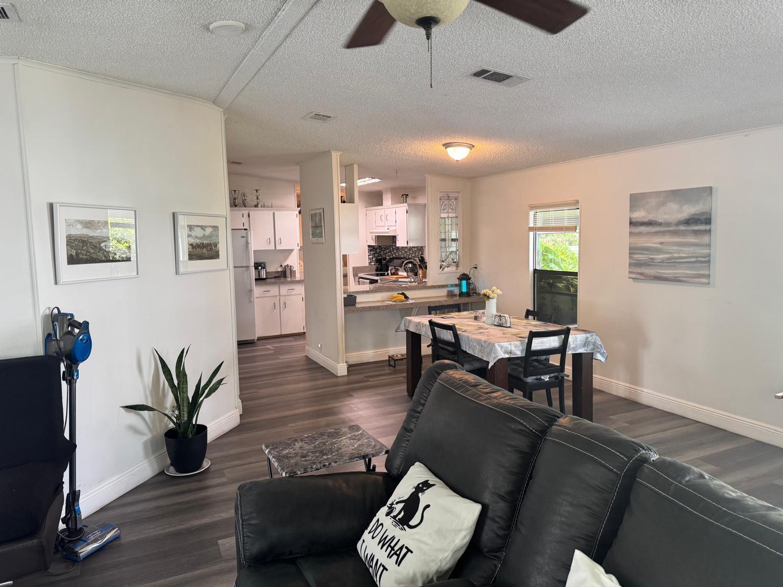 A living room with gray wood-look flooring opens to a dining area and white kitchen — 6059 Palm Harbour Drive, Atlantis FL 33462, ATLANTIS, FL