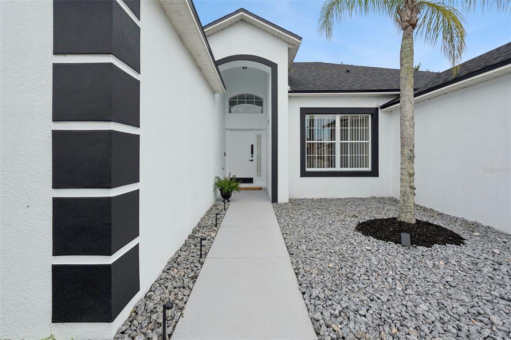 A white house exterior features a concrete walkway leading to a front door with black trim — 2529 JASMINE TRACE DRIVE, KISSIMMEE, FL
