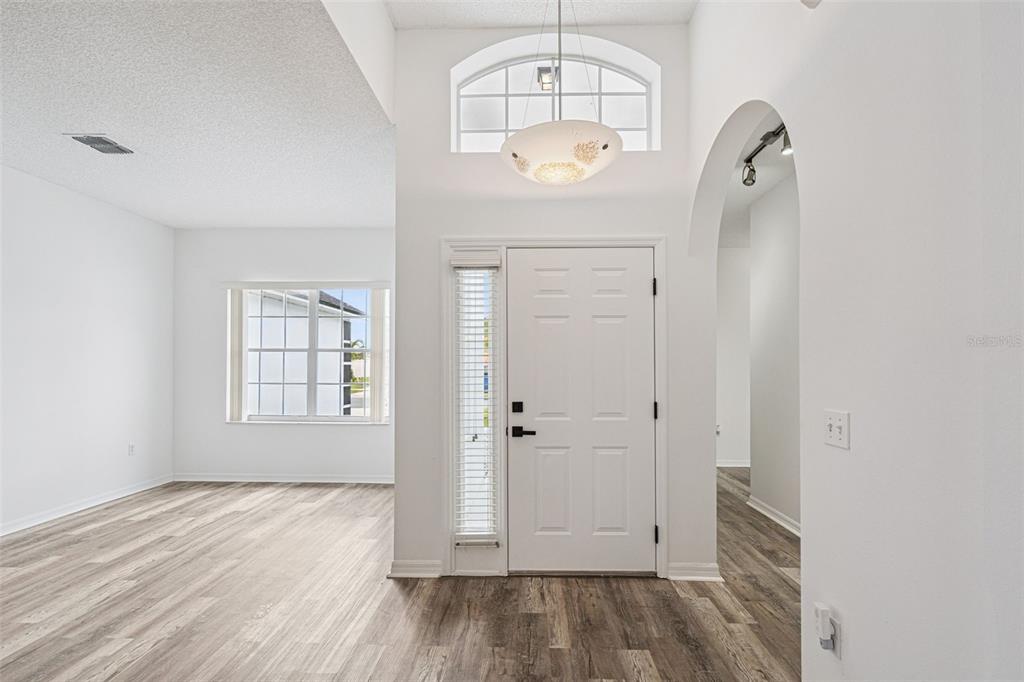 An entryway with light wood-look flooring, a white front door, and a high arched ceiling — 2529 JASMINE TRACE DRIVE, KISSIMMEE, FL
