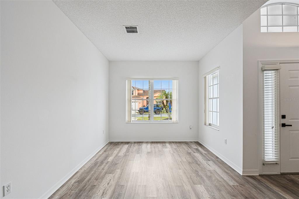 A bright living room features white walls, wood-look flooring, arched entryways, and a front door — 2529 JASMINE TRACE DRIVE, KISSIMMEE, FL