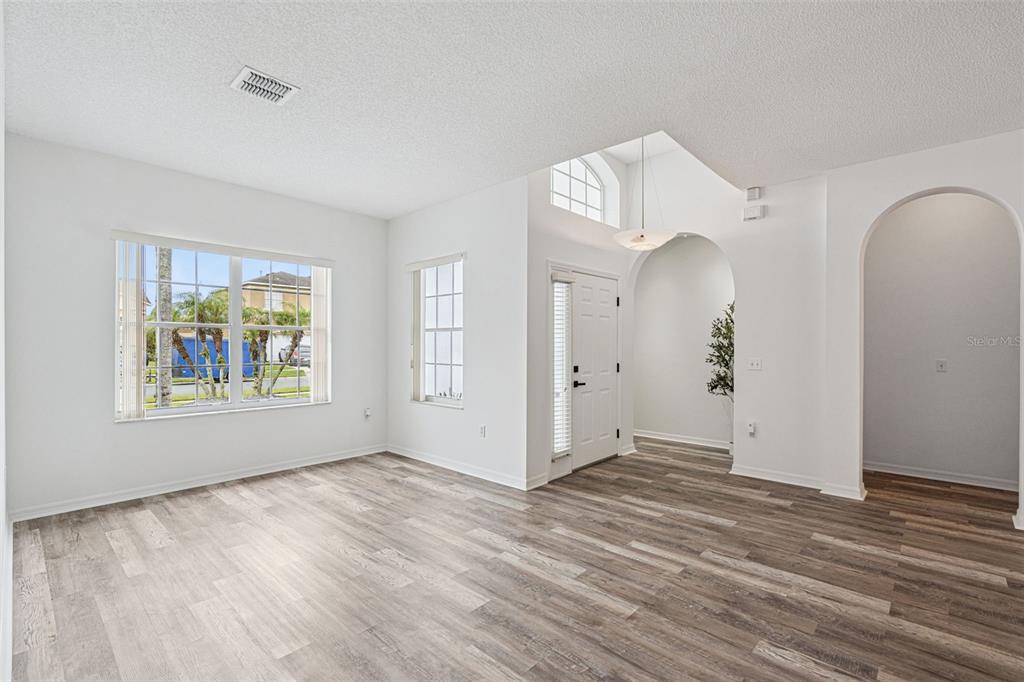 An open-concept living area features wood-look flooring, a chandelier, and an arched entryway to a kitchen — 2529 JASMINE TRACE DRIVE, KISSIMMEE, FL