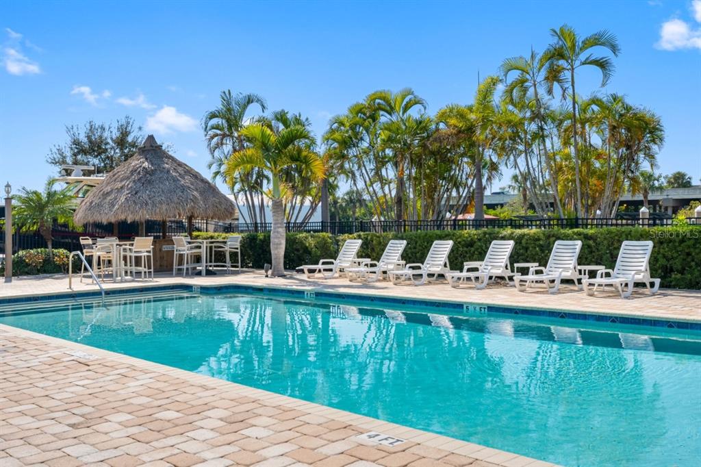 A swimming pool with a tiki hut and lounge chairs on a paved patio — 6057 MOORINGS DRIVE S, ST PETERSBURG, FL